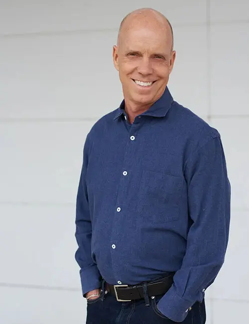 A man in blue shirt standing next to white wall.