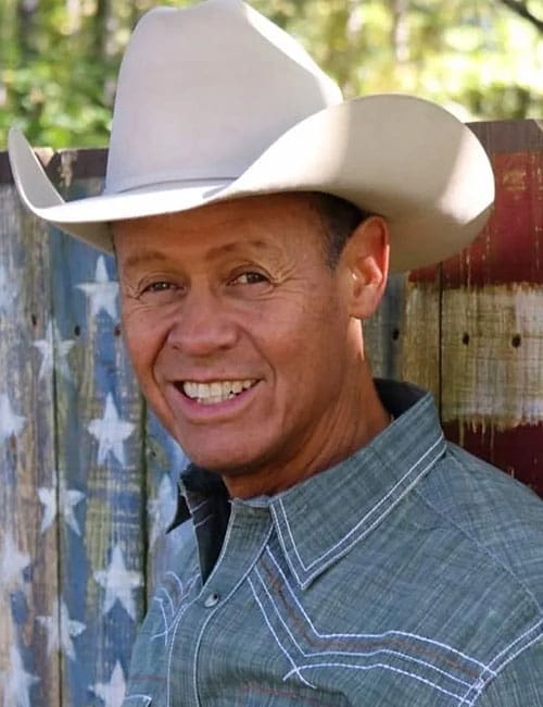 A man in cowboy hat standing next to an american flag.