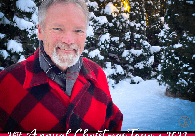 A man in red jacket standing next to snow covered trees.